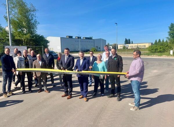 Bild vergr&ouml;&szlig;ern: Minister Sven Schulze (links Bildmitte) und B�rgermeister Sven Hause (rechts Bildmitte) durchschneiden vor den Augen von Unternehmensvertretern und Ratsmitgliedern sowie Vertretern des AZV Saalem�ndung das obligatorische Band zur offiziellen Freigabe der grundhaften sanierten Ringstra�e im IPC Calbe.